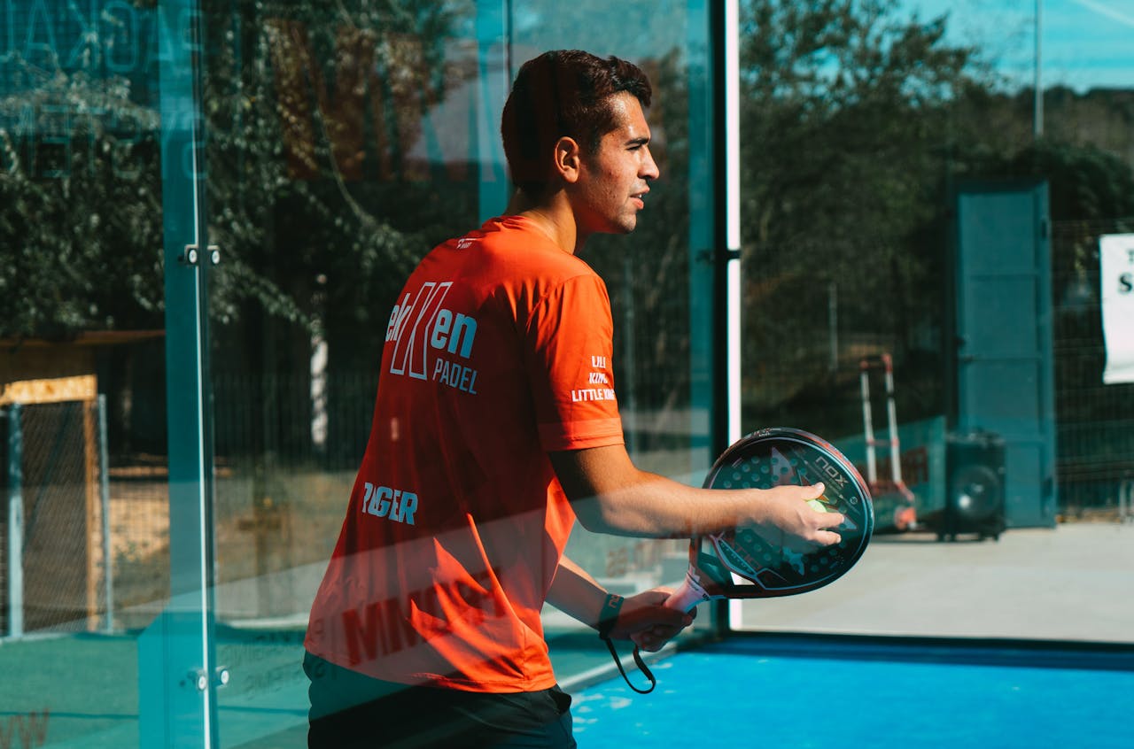 about-us A focused young man practices padel tennis outdoors on a sunny day, showcasing skill and concentration.